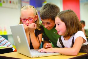 Three children look at a laptop together.