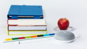 Image of school books, a tablet, apple, and smart speaker.